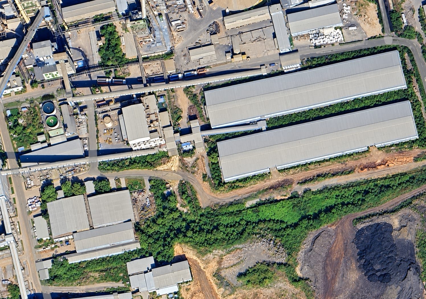 Aerial view of a plant complex with two long storage sheds and conveyor galleries